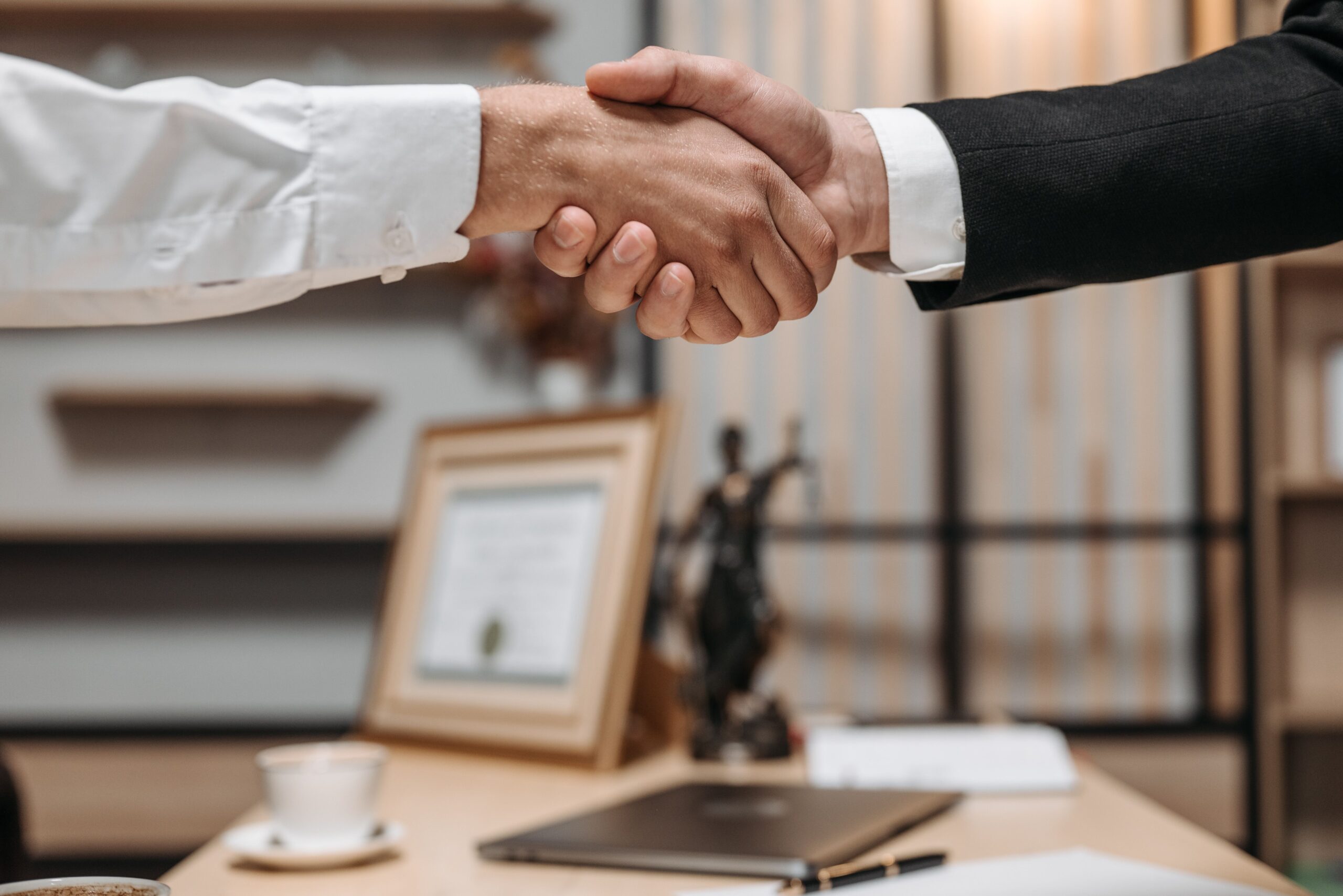 Primo piano di una stretta di mano tra due operatore immobiliare e investitore in un ambiente d'ufficio moderno, enfatizzando partnership e fiducia negli investimenti immobiliari